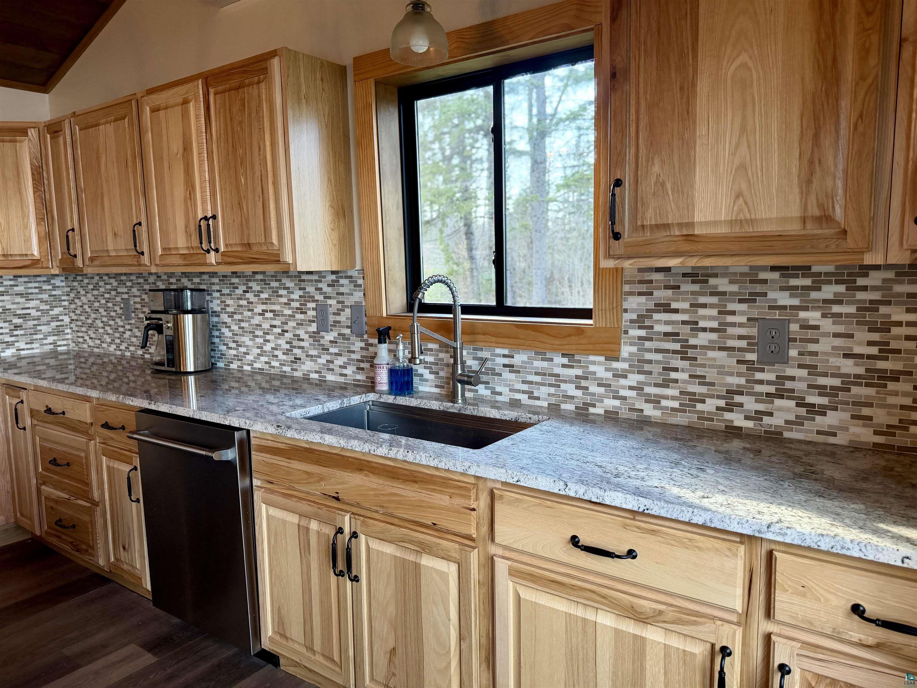 5274 Marble Lake Road Two Harbors, MN 55616 - Photo 21 of 79 Kitchen featuring light wood cabinetry with black hardware, granite countertops, a mosaic tile backsplash, a stainless steel sink with a high-arc faucet, and a built-in stainless steel dishwasher