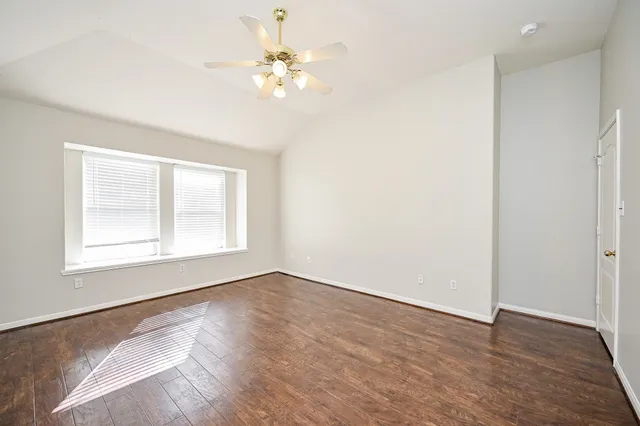 an empty room with wooden floor chandelier fan and windows
