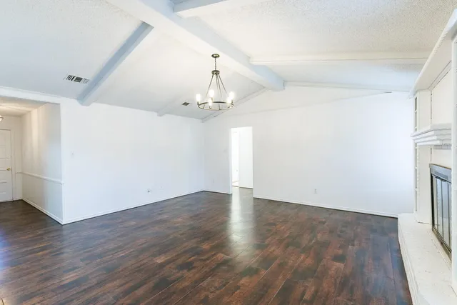 an empty room with wooden floor fireplace and chandelier fan