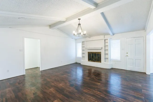 an empty room with wooden floor fireplace and windows