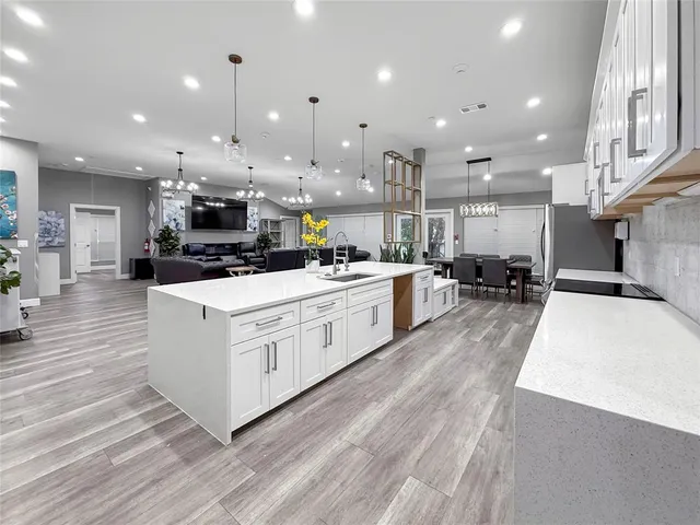 a kitchen with stainless steel appliances kitchen island granite countertop a stove a sink a refrigerator and white cabinets with wooden floor