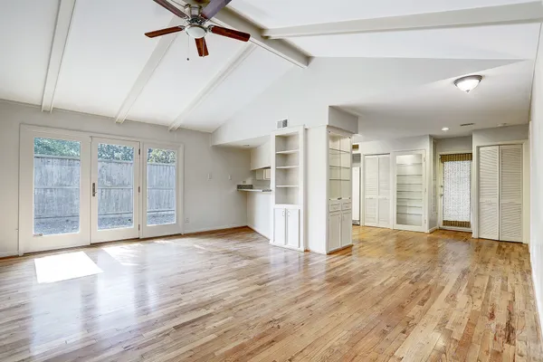 a view of an empty room with wooden floor and a ceiling fan