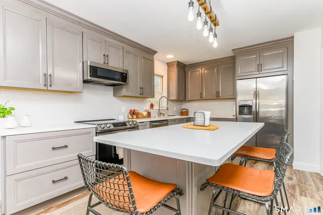 a kitchen with stainless steel appliances a stove a sink dishwasher a refrigerator with white cabinets and wooden floor