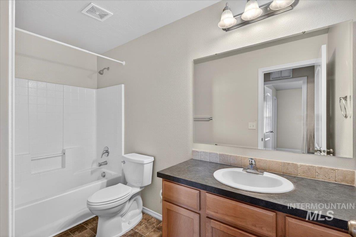 1555 Condor Drive Middleton, ID 83644 - Photo 35 of 50 Bathroom featuring a shower-tub combination with white subway tile surround, a built-in vanity with a dark countertop and wood-finish cabinetry, a rectangular mirror, and an overhead vanity light fixture