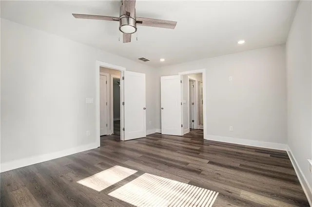 a view of an empty room with wooden floor and fan