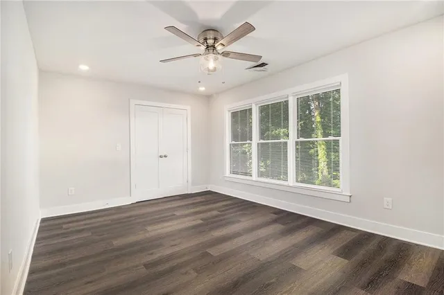 an empty room with wooden floor chandelier fan and windows