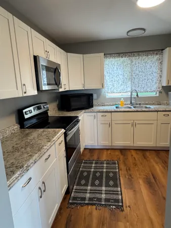 a kitchen with granite countertop a stove a sink dishwasher and a microwave oven with white cabinets