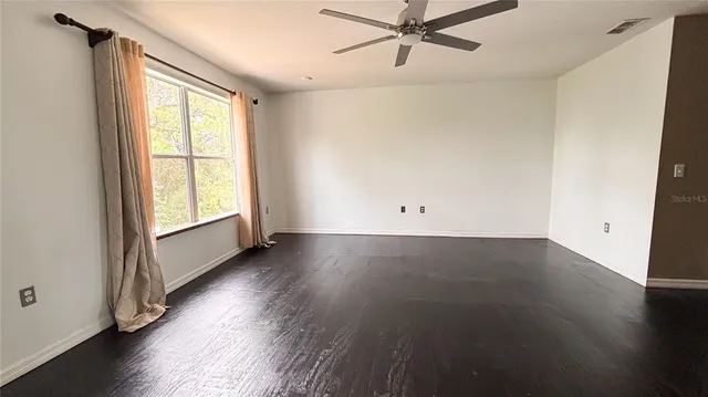 an empty room with wooden floor fan and windows