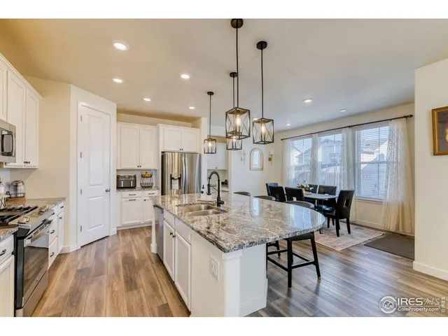 a open kitchen with kitchen island a refrigerator a stove a sink a dining table and chairs with wooden floor