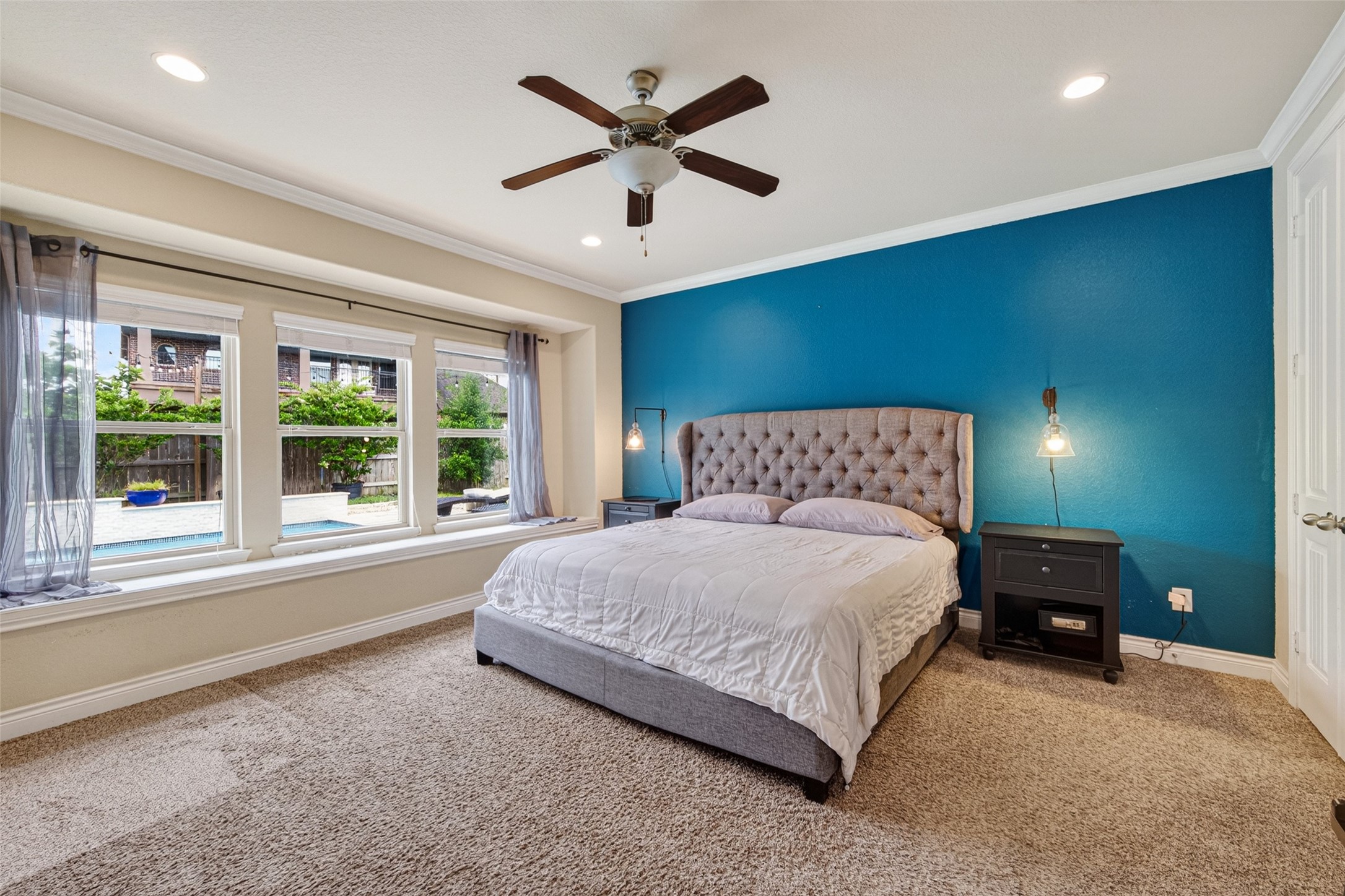 25611 Ellis Ridge Court Katy, TX 77494 - Photo 40 of 49 This spacious bedroom features a bold blue accent wall, plush carpet, and a ceiling fan. Large windows overlook a serene backyard with a pool, bringing in ample natural light.
