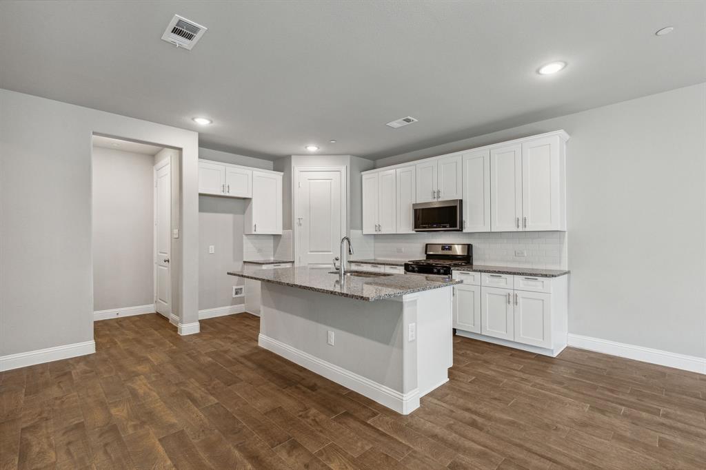 a kitchen with stainless steel appliances a stove top oven a sink a refrigerator white cabinets and wooden floor