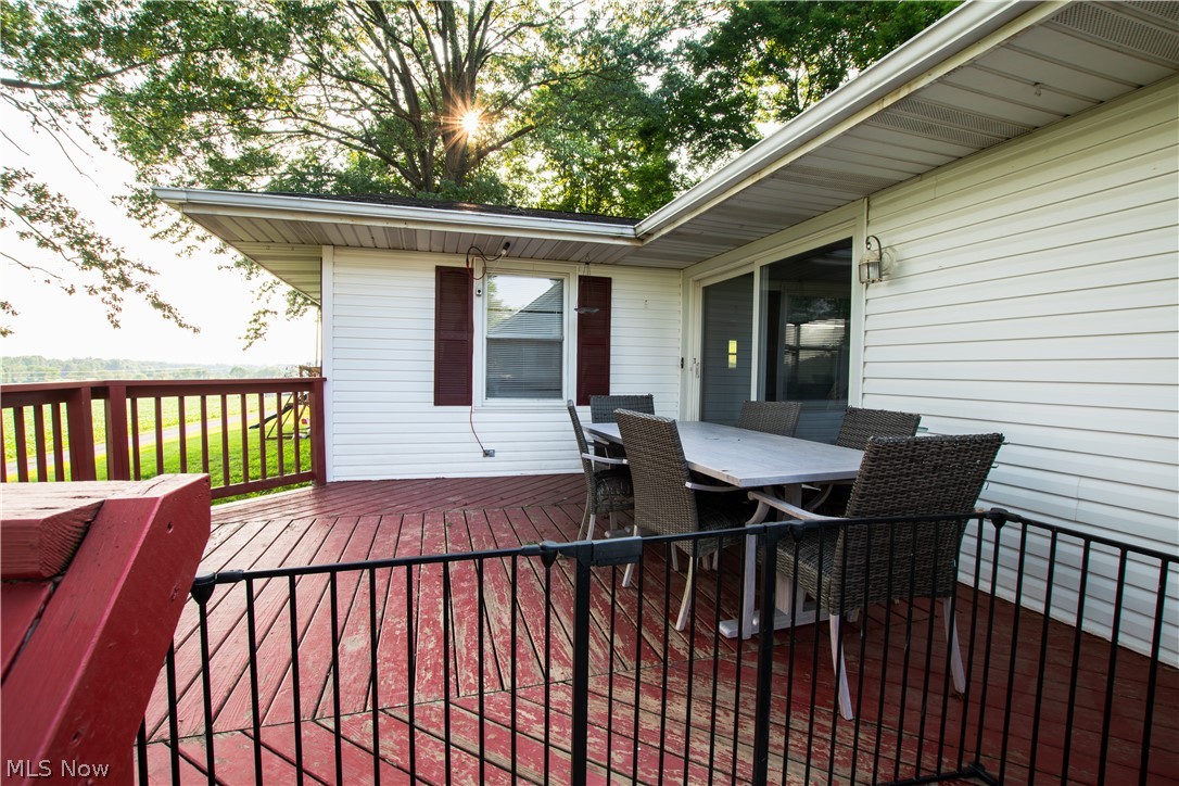 1757 Pleasant Valley Road Northeast New Philadelphia, OH 44663 - Photo 10 of 33 Spacious outdoor deck featuring red-stained wooden planks and railing, white vinyl siding, a sliding glass door, and a single window with burgundy shutters