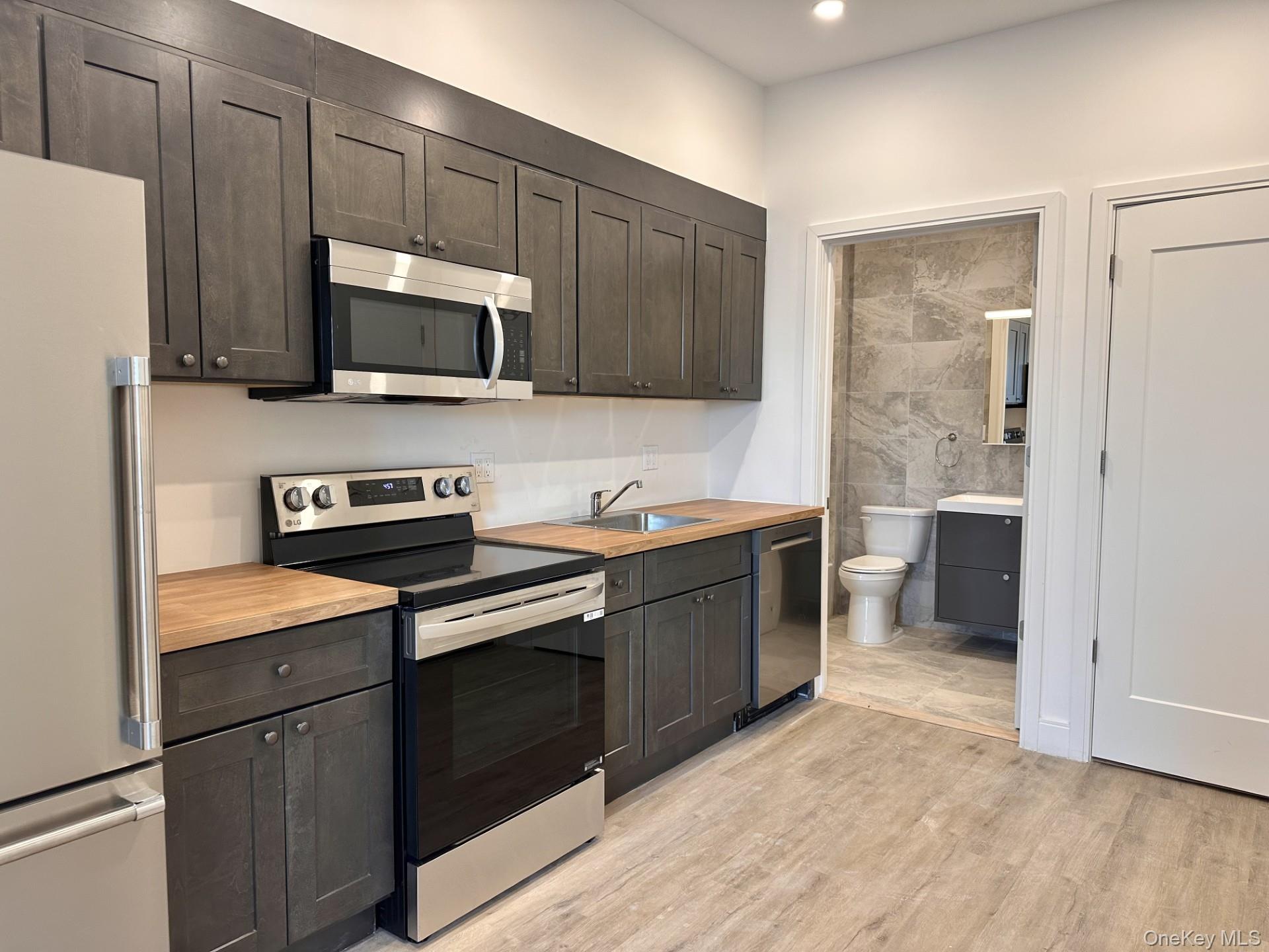 Kitchen with stainless steel appliances, light wood finished floors, wood counters, and dark brown cabinetry
