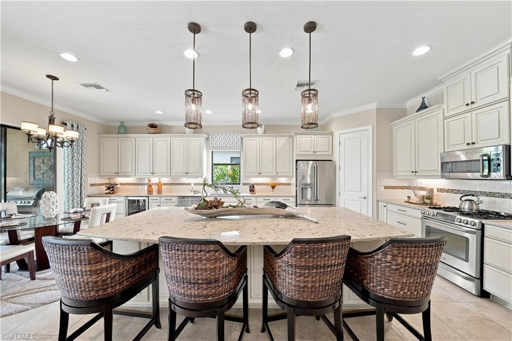 9256 Rialto Lane Naples, FL 34119 - Photo 9 of 43 Open-concept kitchen and dining area featuring white shaker-style cabinetry, a large kitchen island with pendant lighting, stainless steel appliances, and tile flooring