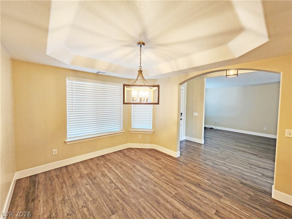 4591 Stoneham Street Pahrump, NV 89061 - Photo 18 of 42 A well-lit dining area featuring a tray ceiling, modern chandelier, and rich wood-look flooring.