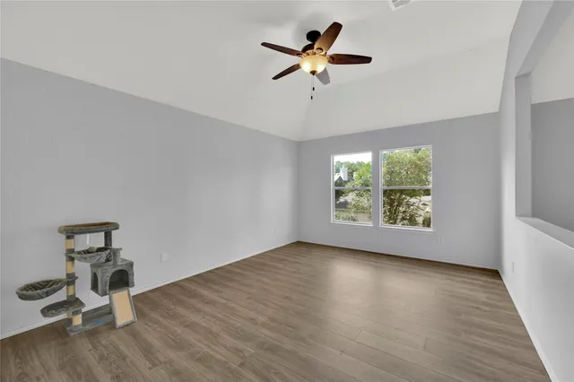 an empty room with wooden floor fan and windows