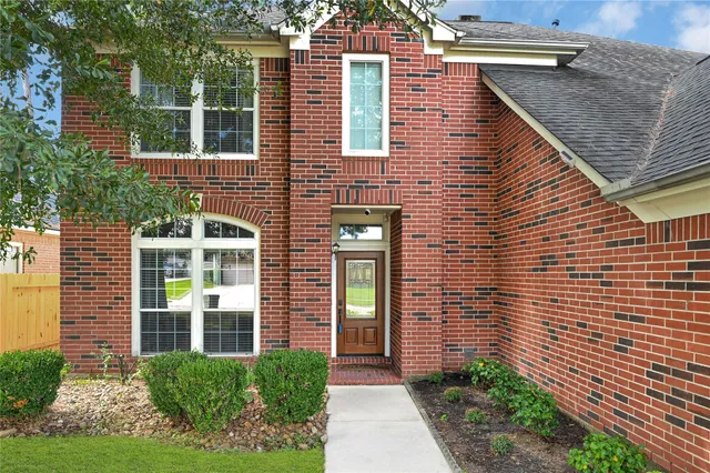 a view of a brick house with a yard potted plants and large tree