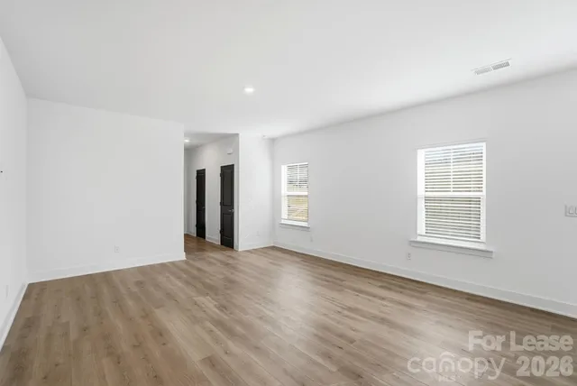 a view of an empty room with wooden floor and windows