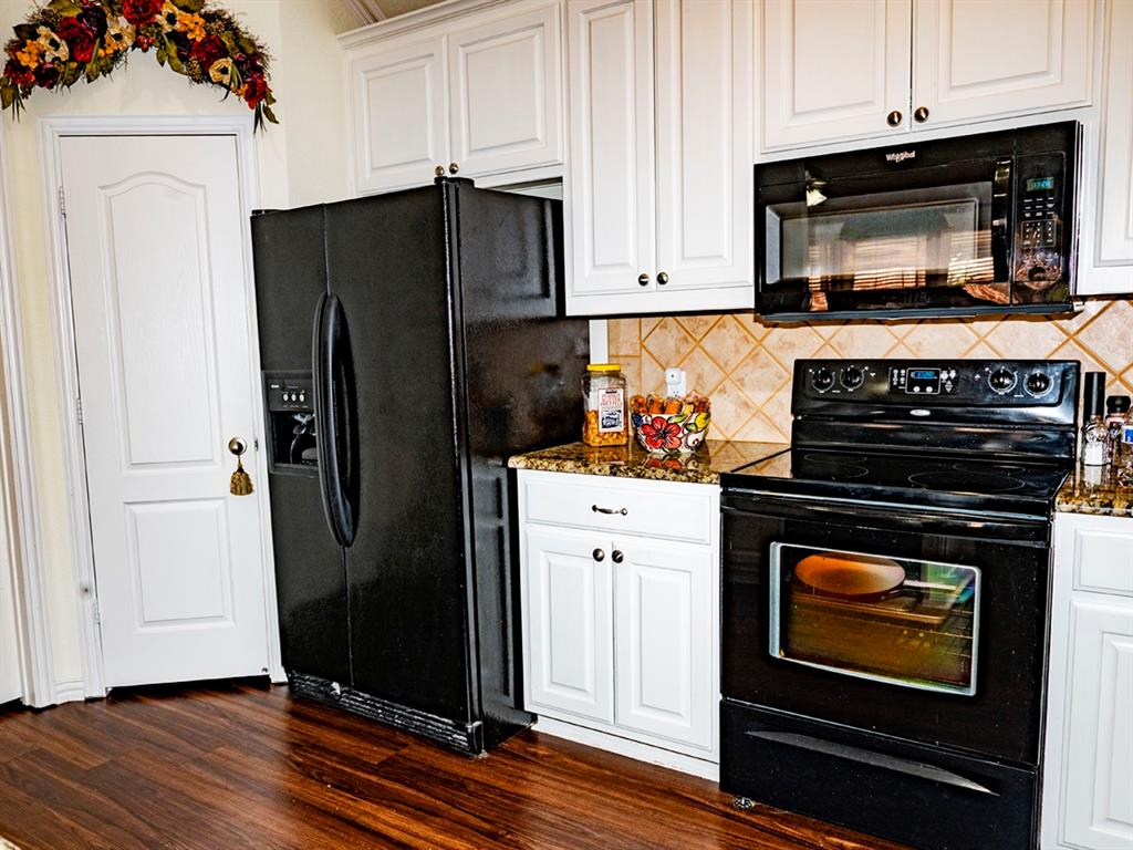 9028 Racquet Club Drive Fort Worth, TX 76120 - Photo 14 of 26 a kitchen with granite countertop a refrigerator stove and white cabinets with wooden floor
