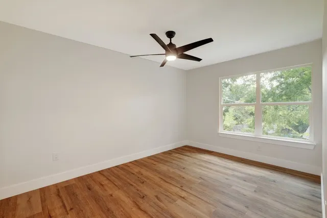 an empty room with wooden floor fan and windows