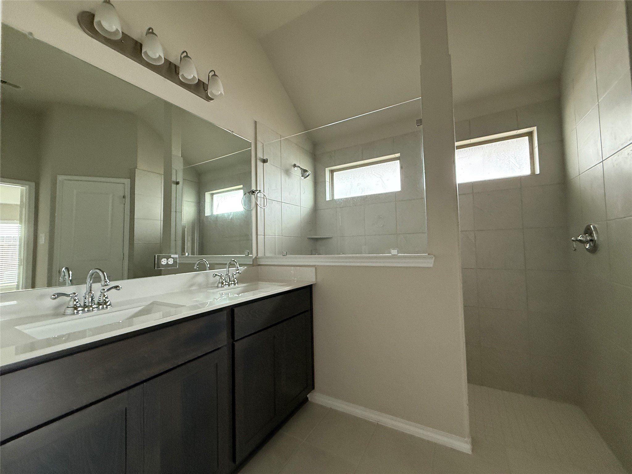 31961 Retama Rnch Drive Spring, TX 77386 - Photo 22 of 25 Modern bathroom with a double vanity, sleek dark cabinetry, and a large mirror. Features a spacious walk-in shower with tile walls and natural light from high windows.