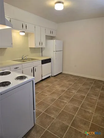 a kitchen with granite countertop a sink a stove a refrigerator and white cabinets