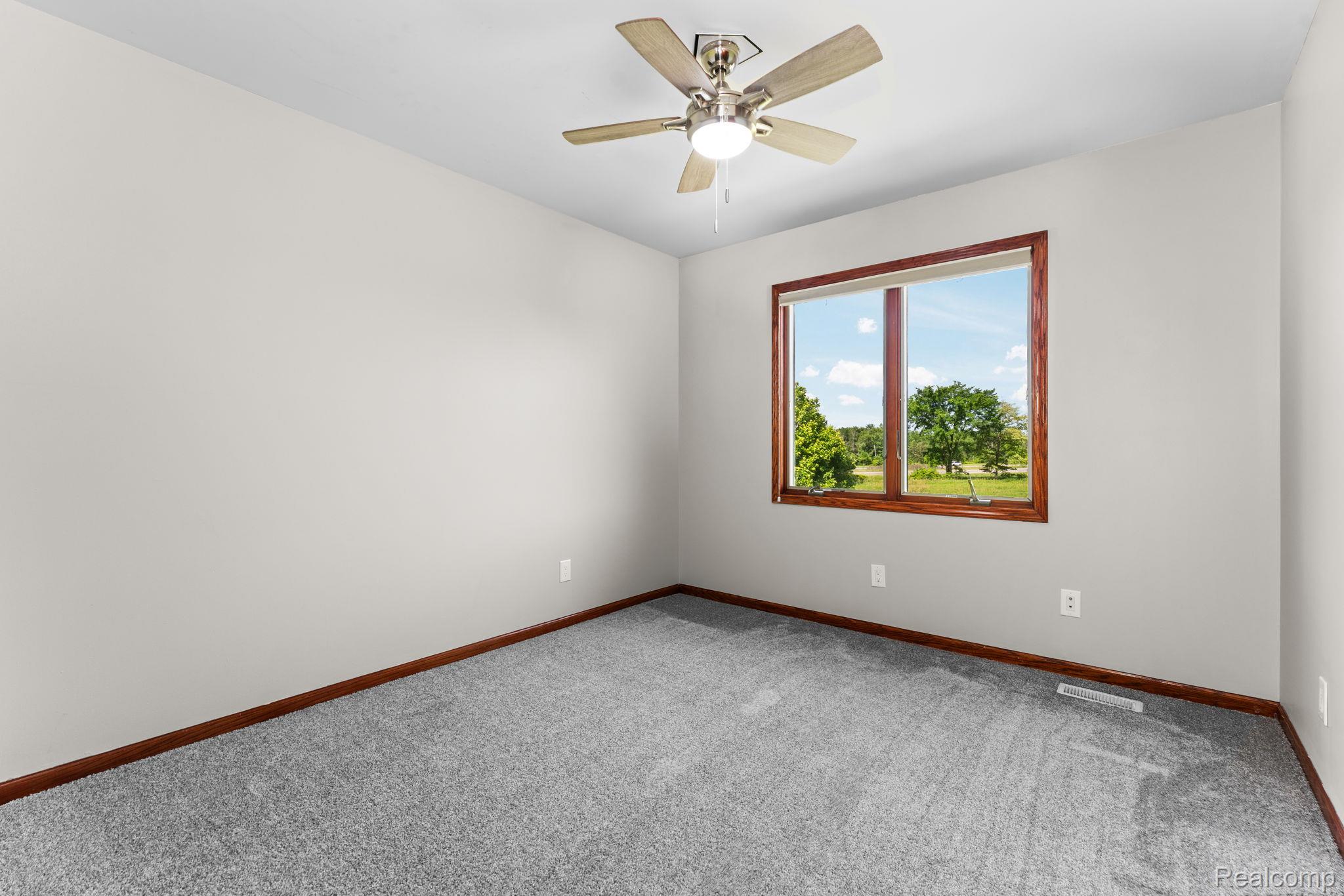 2381 Burke Road Fowlerville, MI 48836 - Photo 20 of 31 Bedroom 3, featuring a ceiling fan with light fixture, a wood-trimmed window, gray carpeting, and light-toned walls