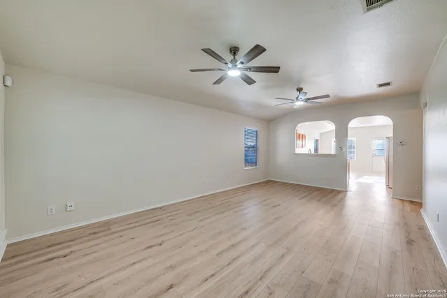 an empty room with wooden floor fan and windows