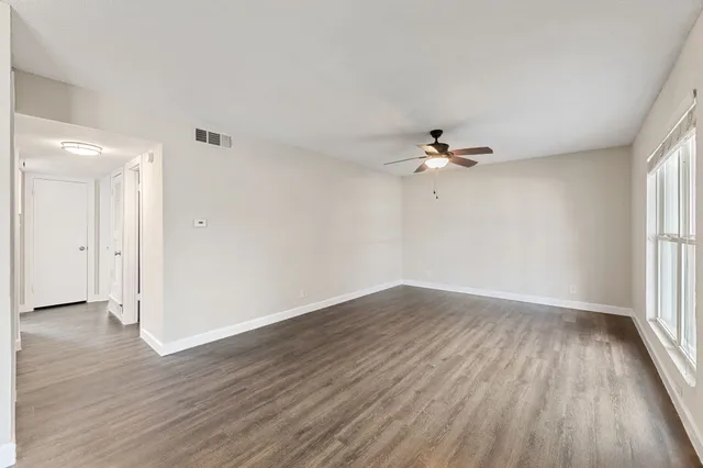 an empty room with wooden floor fan and windows