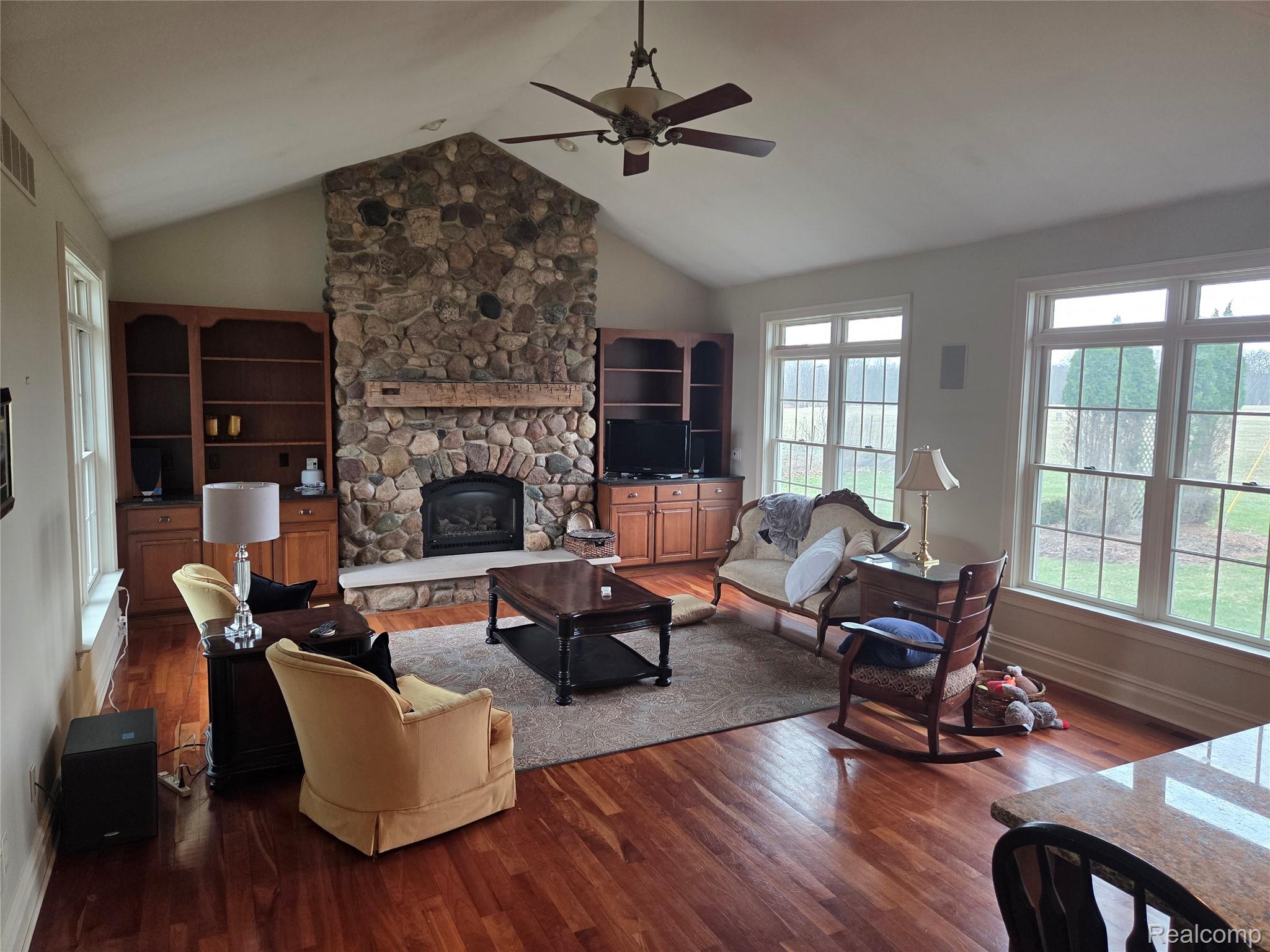 900 South Maxfield Road Brighton, MI 48114 - Photo 15 of 30 Living area with a stone fireplace, ceiling fan, and dark wood-type flooring