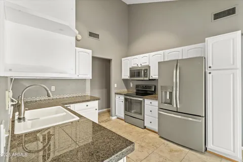 a kitchen with stainless steel appliances granite countertop a refrigerator a stove a sink and white cabinets with wooden floor