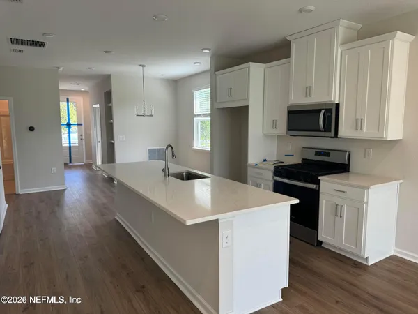 a kitchen with stainless steel appliances a stove top oven a sink a refrigerator white cabinets and wooden floor