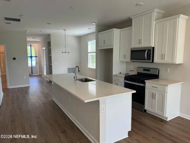 a kitchen with stainless steel appliances a stove top oven a sink a refrigerator white cabinets and wooden floor