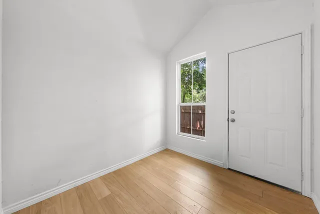 a view of an empty room with wooden floor and a window