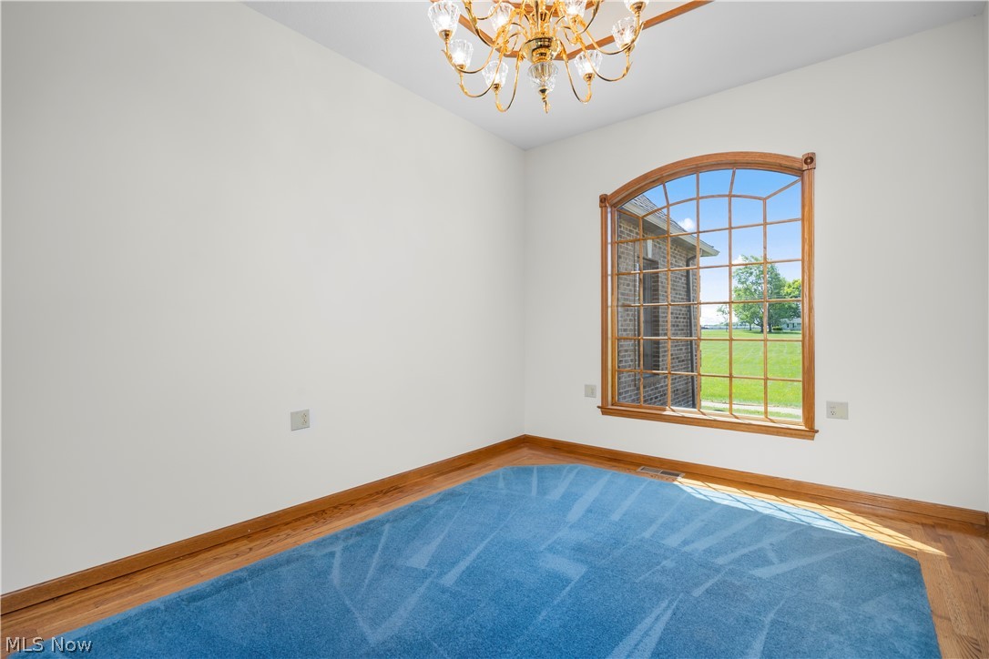 51488 Peck Wadsworth Road Wellington, OH 44090 - Photo 13 of 50 Room featuring an arched grid window with wood trim, a decorative chandelier, white walls, and wood-finish flooring with a partial blue carpet inlay