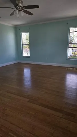an empty room with wooden floor fan and windows