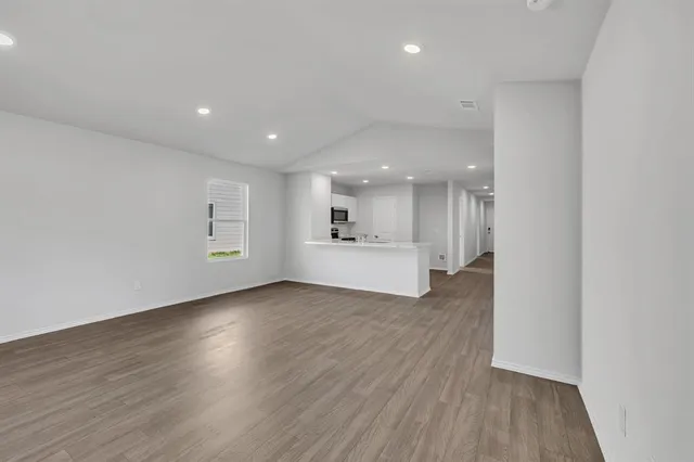 a view of an empty room with wooden floor kitchen view and a window