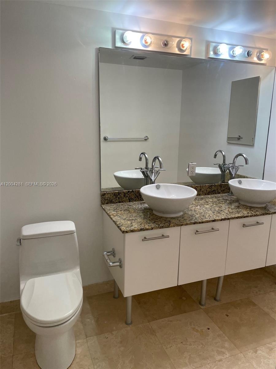 41 Southeast 5th Street, Unit 1614 Miami, FL 33131 - Photo 12 of 23 a bathroom with a granite countertop toilet a sink and a mirror