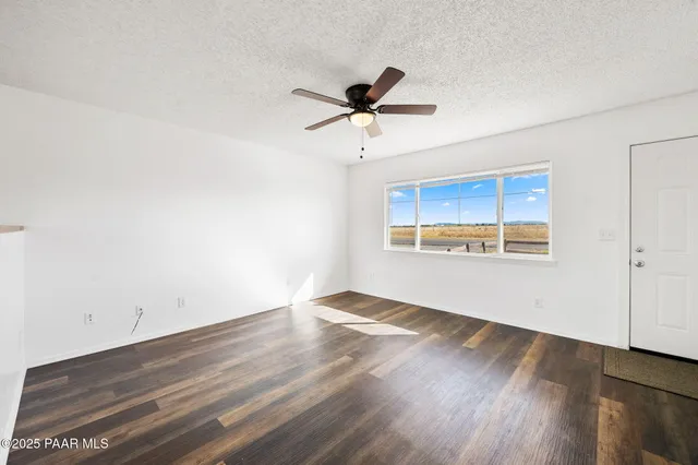 a view of an empty room with wooden floor and a ceiling fan