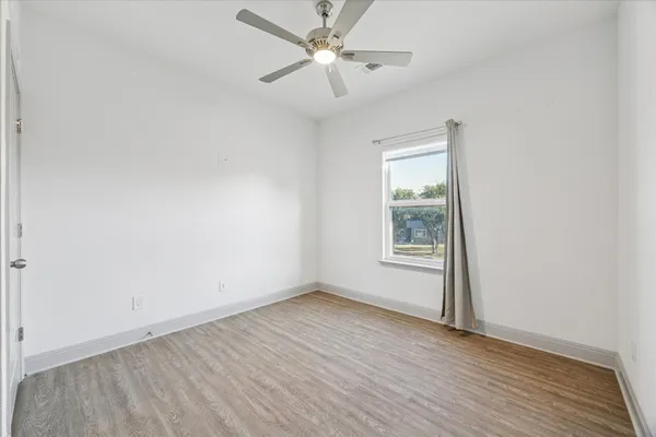 an empty room with wooden floor chandelier fan and windows