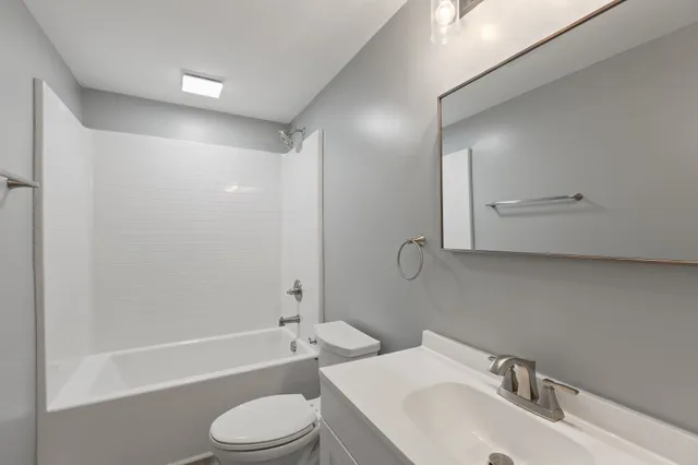 a bathroom with a bathtub shower sink vanity mirror and toilet