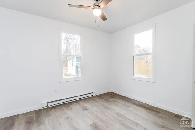 an empty room with wooden floor fan and windows