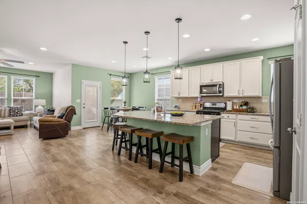 a large kitchen with stainless steel appliances kitchen island granite countertop a refrigerator a stove a sink a dining table and chairs with wooden floor