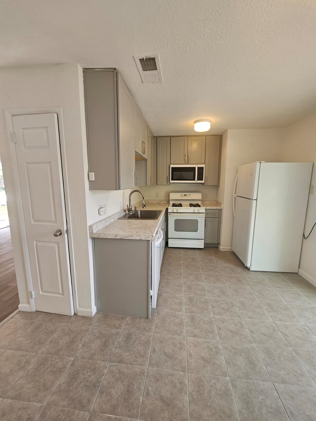 1401 Trinity Street Lockhart, TX 78644 - Photo 8 of 31 Kitchen featuring light gray cabinetry, light-toned countertops, tile flooring, and integrated white appliances including a range, dishwasher, and microwave