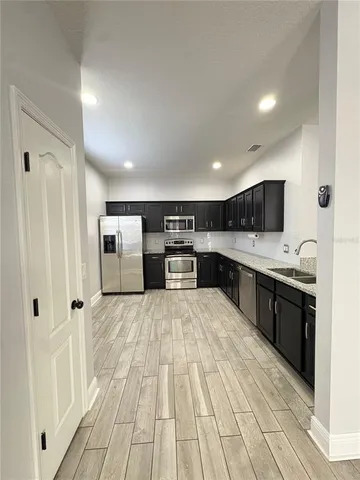 a large white kitchen with stainless steel appliances granite countertop a lot of cabinets and wooden floor