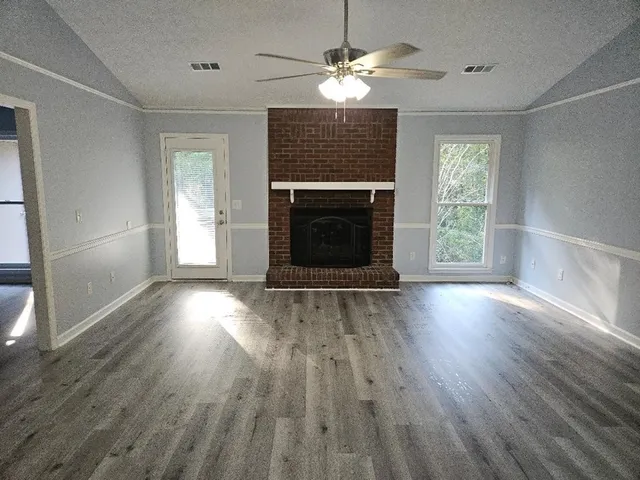 an empty room with wooden floor fireplace and windows