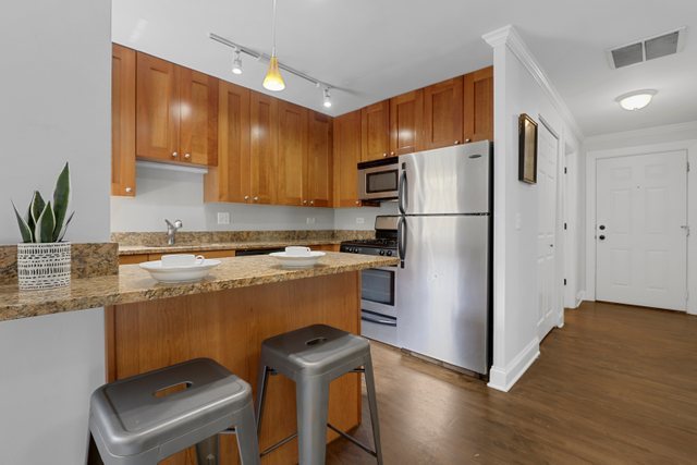4144 North Sheridan Road, Unit 208 Chicago, IL 60613 - Photo 9 of 24 a kitchen with granite countertop a refrigerator a sink a stove and wooden floor