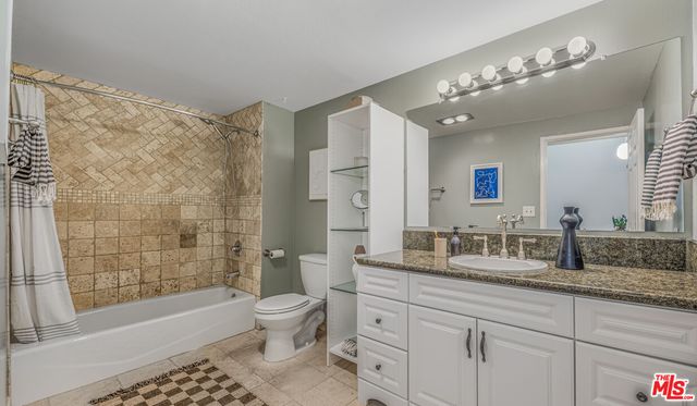 a bathroom with a granite countertop sink a toilet a mirror a vanity a bathtub and shower