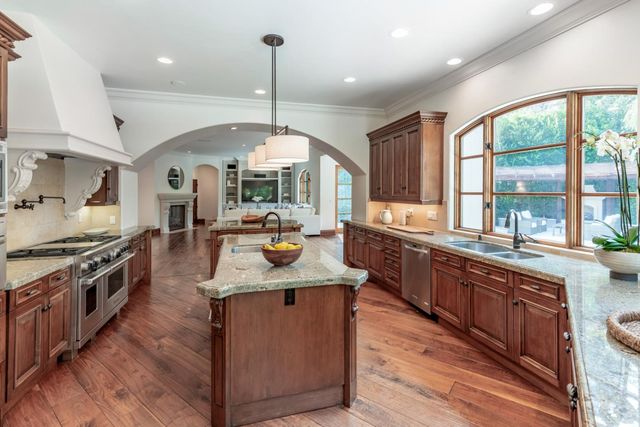 a kitchen with stainless steel appliances granite countertop a stove a sink dishwasher a refrigerator and a dining table with wooden floor