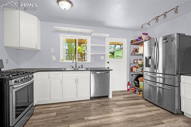 605 Huron Road Colorado Springs, CO 80910 - Photo 6 of 30 Kitchen with stainless steel appliances, a sink, open shelves, dark countertops, and a textured ceiling
